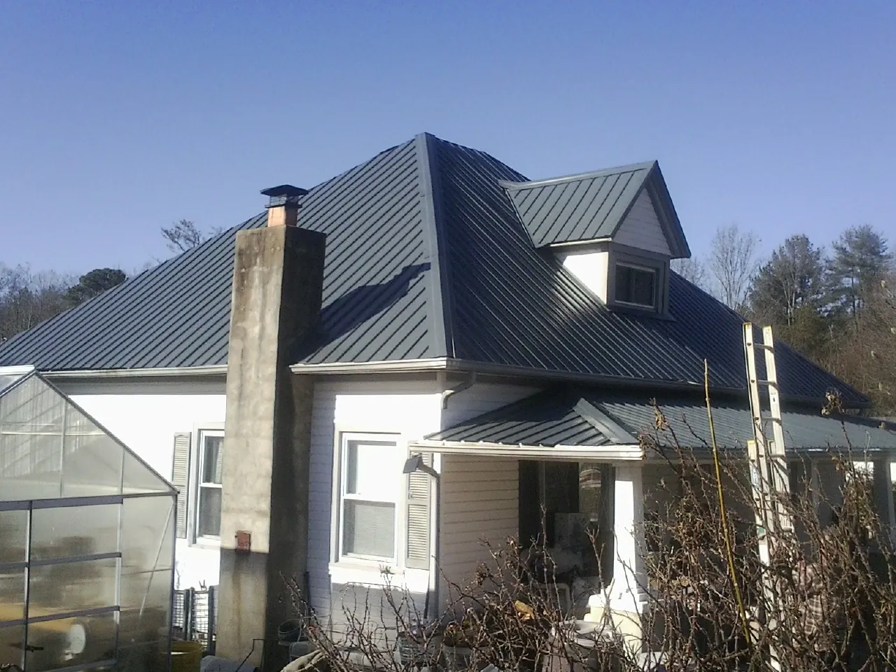 Dark blue standing seam metal roof on a white farmhouse with dormer — Slate & Tile Roof Repair by Roofing Brothers in Saint Pauls