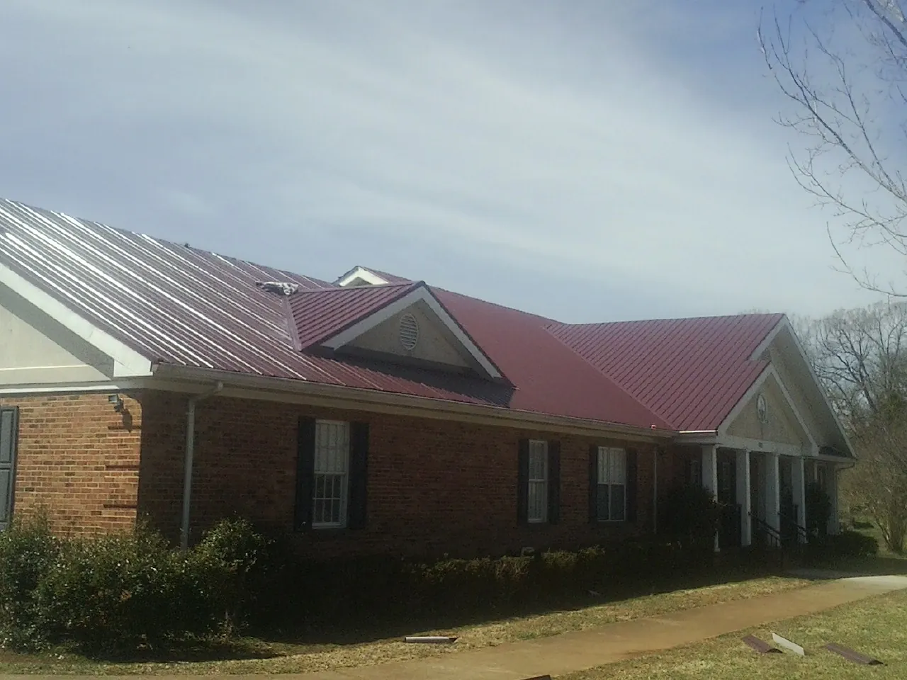 Red metal roof with gabled entries on a long brick building, from a Hail Damage Roof Repair job in Saint Pauls