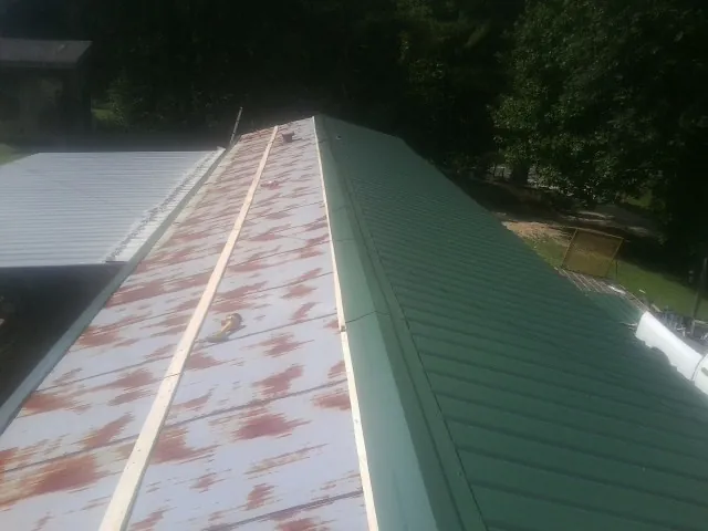 Old rusted panels beside newly installed green metal roofing — Wind Damage Roof Repair by Roofing Brothers in Saint Pauls