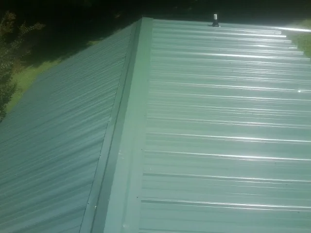 New green metal panels meeting at the ridge of a roof — Flat Roof Repair work by our crew in Saint Pauls