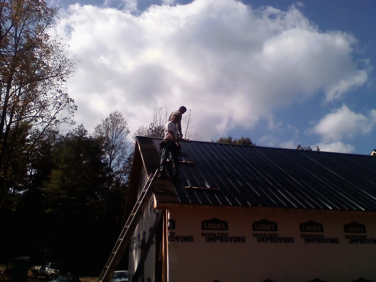 Roofer fastening dark metal panels high against a cloudy sky, from a Roof Inspection job in Saint Pauls