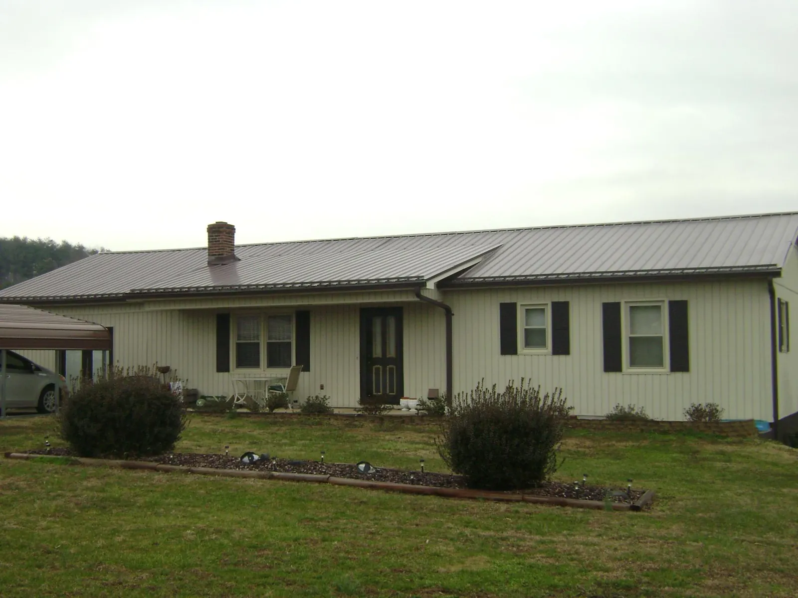 Brown metal roof on a cream sided ranch home with a brick chimney in Saint Pauls