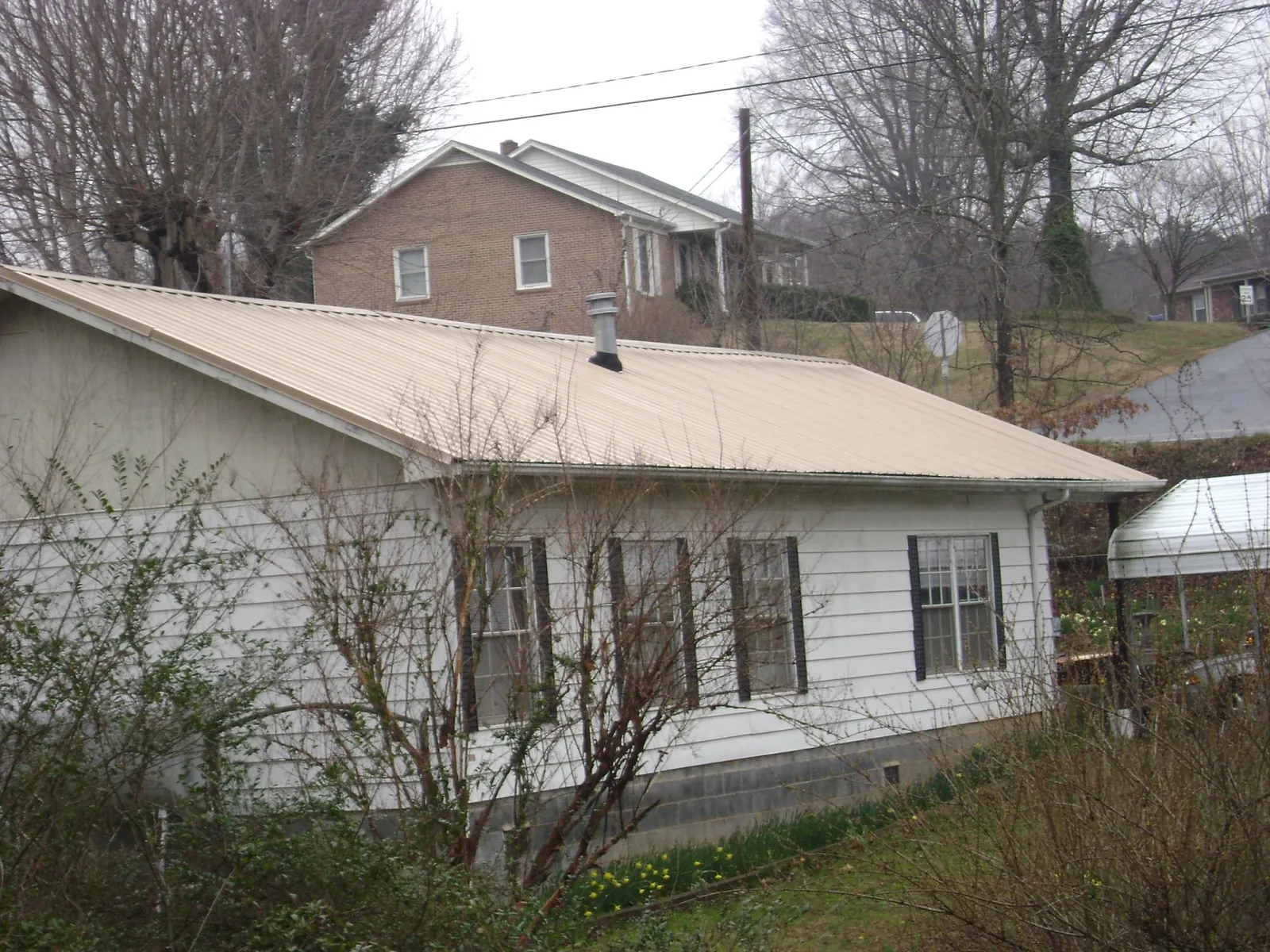 Tan metal roof on a white sided house set into a hillside — Commercial Roofing by Roofing Brothers in Saint Pauls
