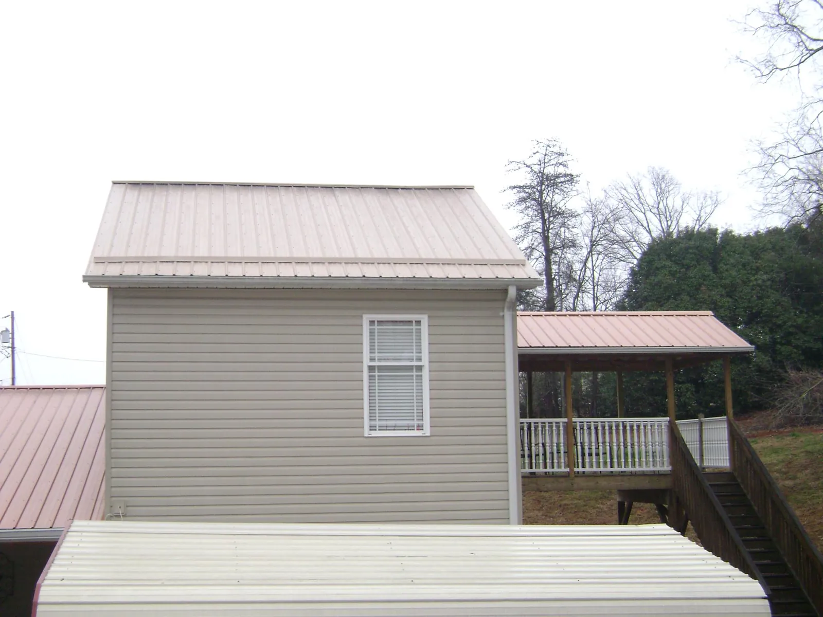 Tan metal roofs on a two story addition and attached porch, from a Roof Replacement job in Saint Pauls